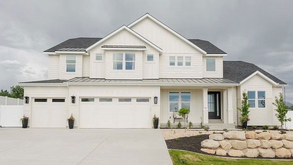 A white house with a garage and stone wall surrounded by grass.